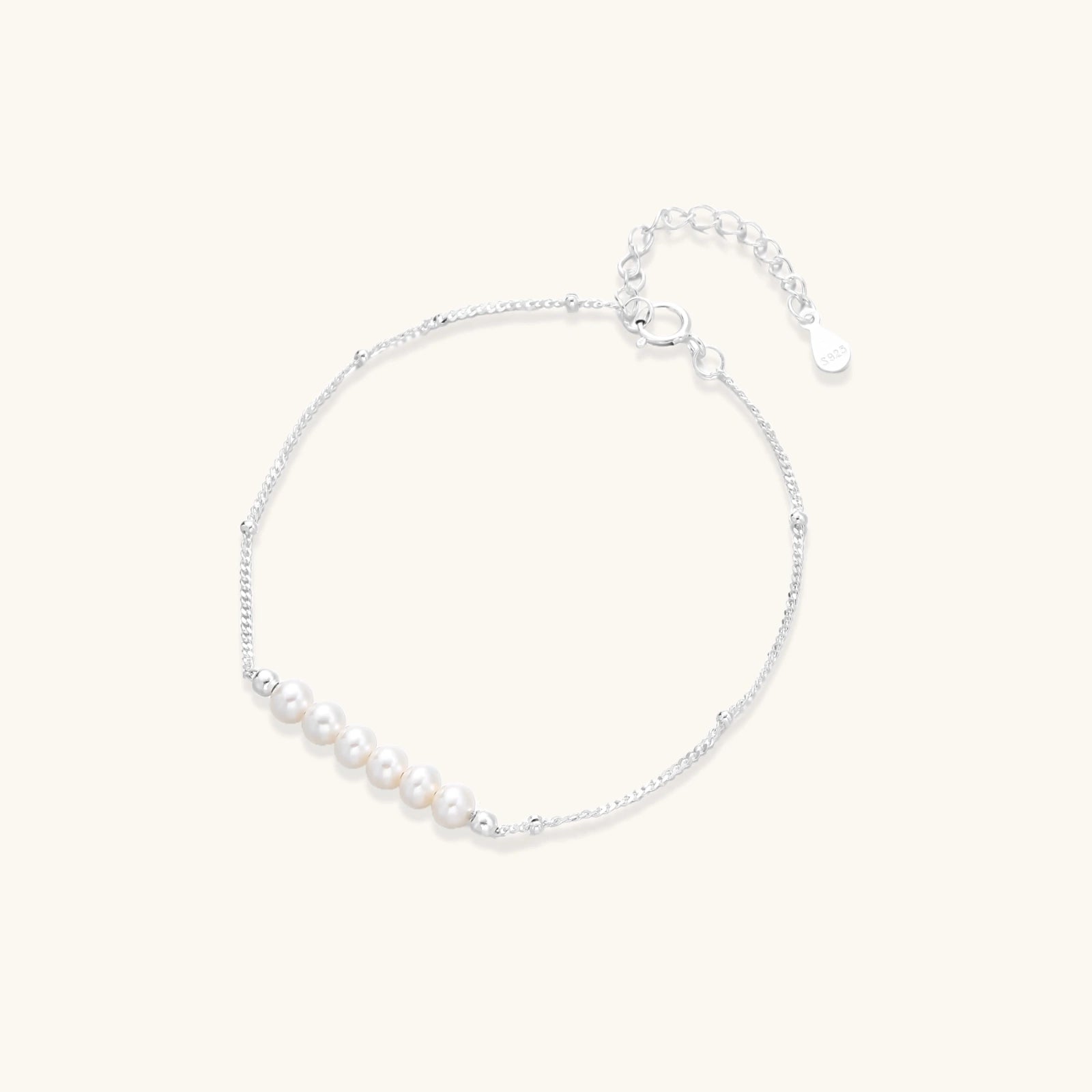 Delicate rhodium-plated silver chain bracelet with row of small baroque pearls centered on white background.