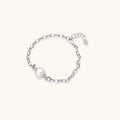 Rhodium-plated silver chain bracelet with single white freshwater pearl and heart charm clasp on cream background