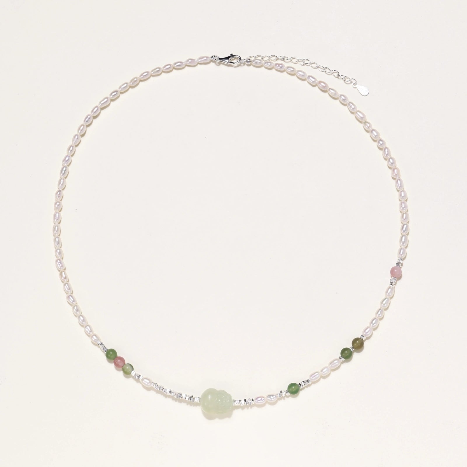 Delicate pearl necklace with pale green serpentine jade centerpiece and colorful agate beads on cream background