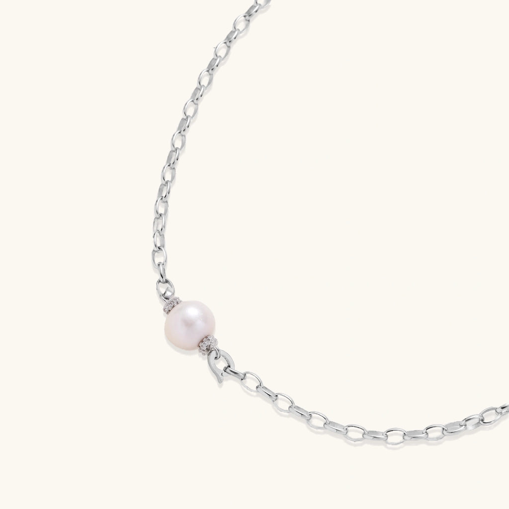 Dainty rhodium-plated silver chain necklace with centered 10mm freshwater pearl and crystal accents on cream background
