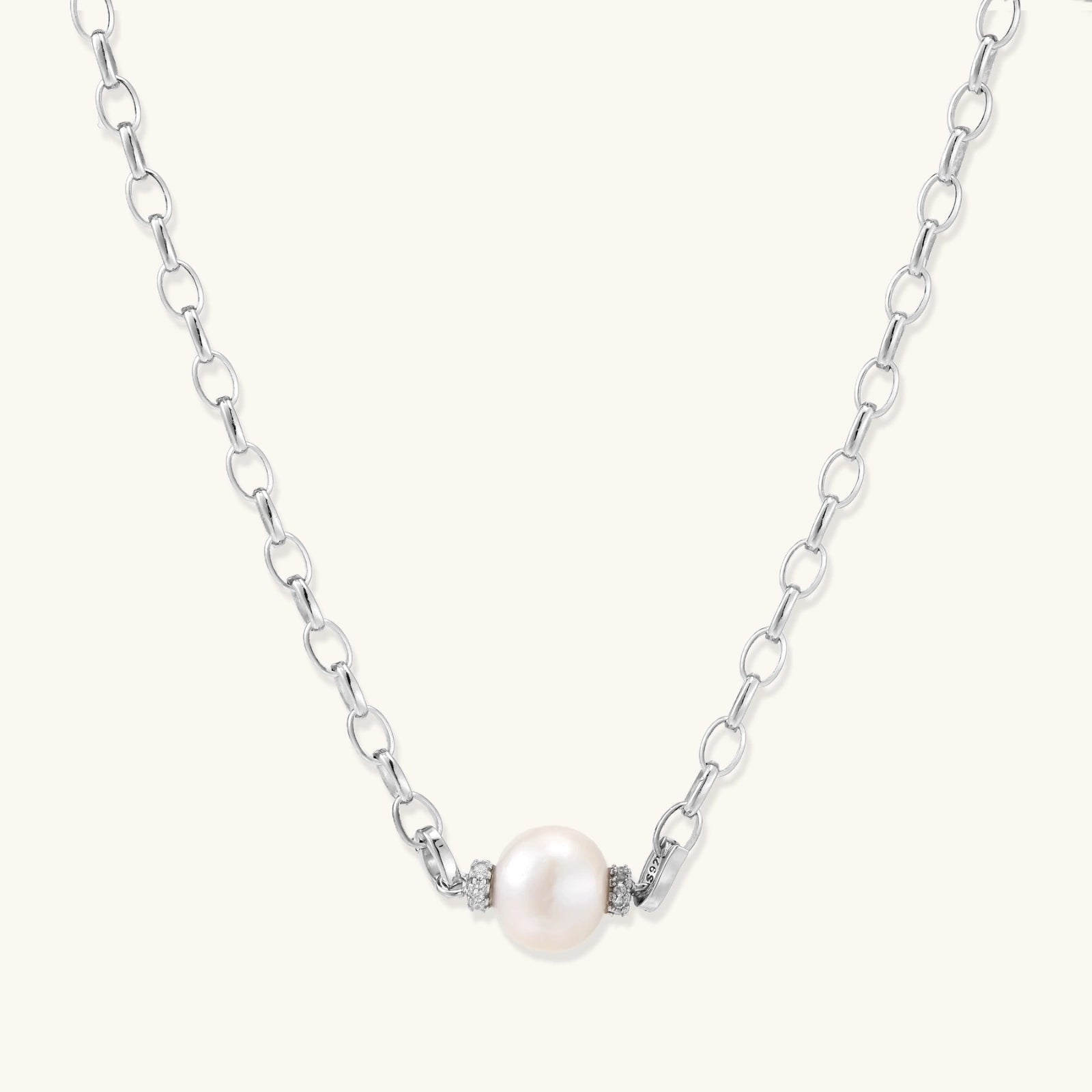 Dainty rhodium-plated silver chain necklace with centered 10mm freshwater pearl and crystal accents on cream background