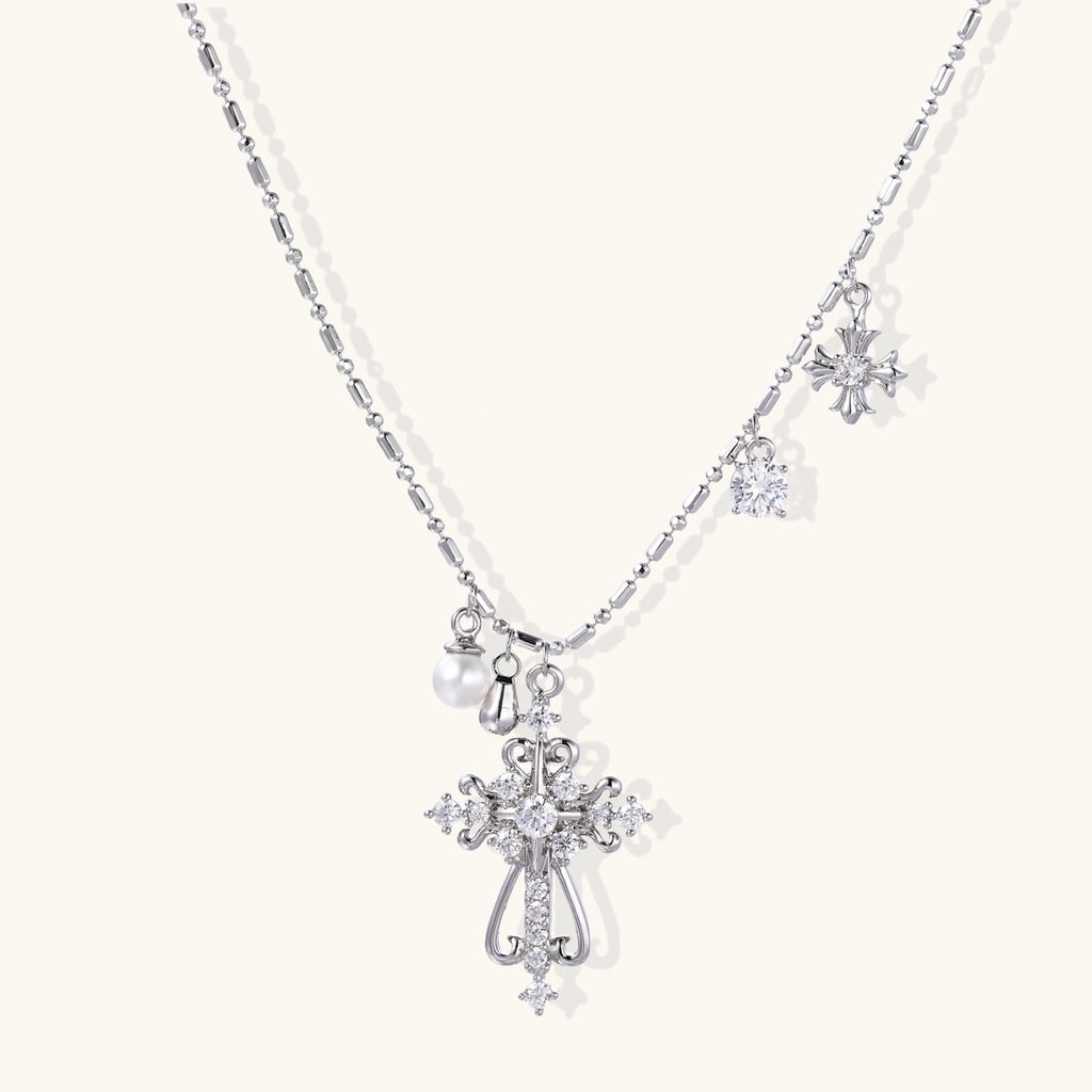 Ornate white gold-plated cross pendant with zirconia stones and pearl accents on adjustable silver chain against cream background