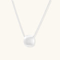 Minimalist brushed sterling silver dome pendant on delicate chain against cream background, showing matte textured finish