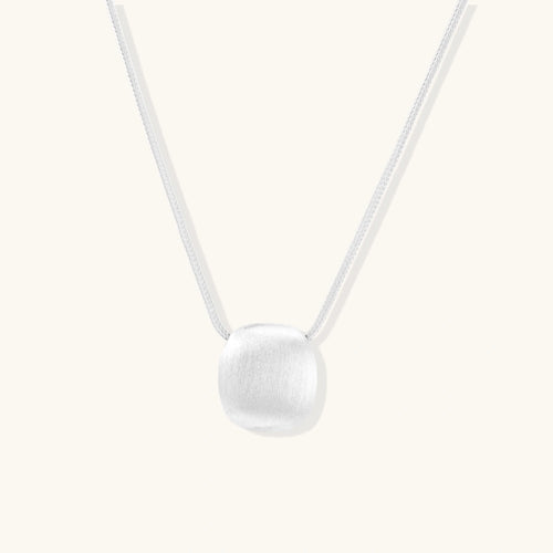 Minimalist brushed sterling silver dome pendant on delicate chain against cream background, showing matte textured finish