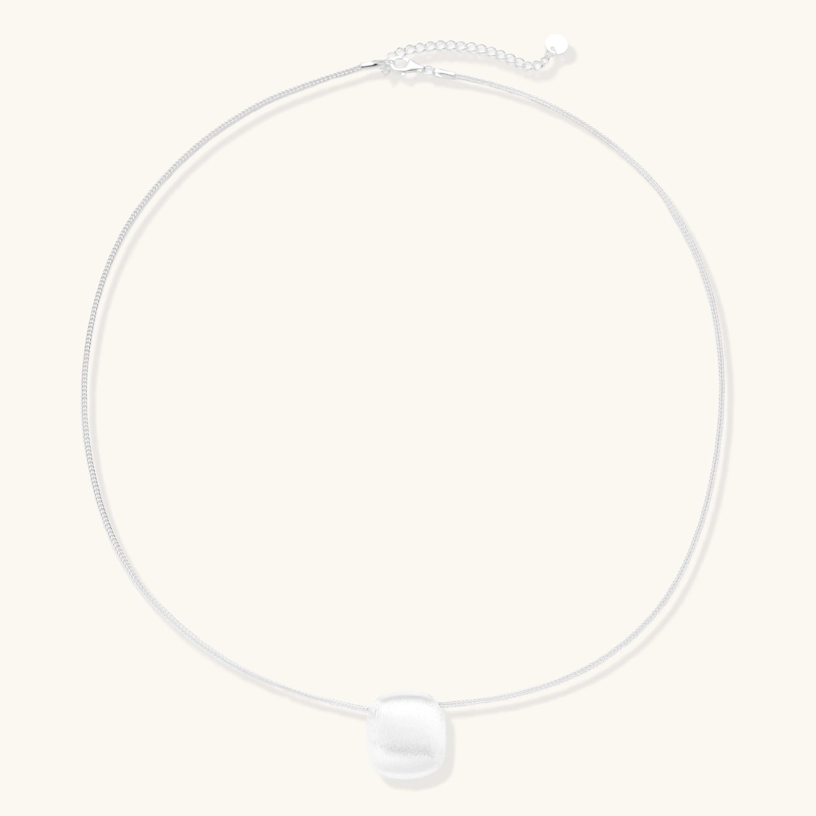 Minimalist brushed sterling silver dome pendant on delicate chain against cream background, showing matte textured finish