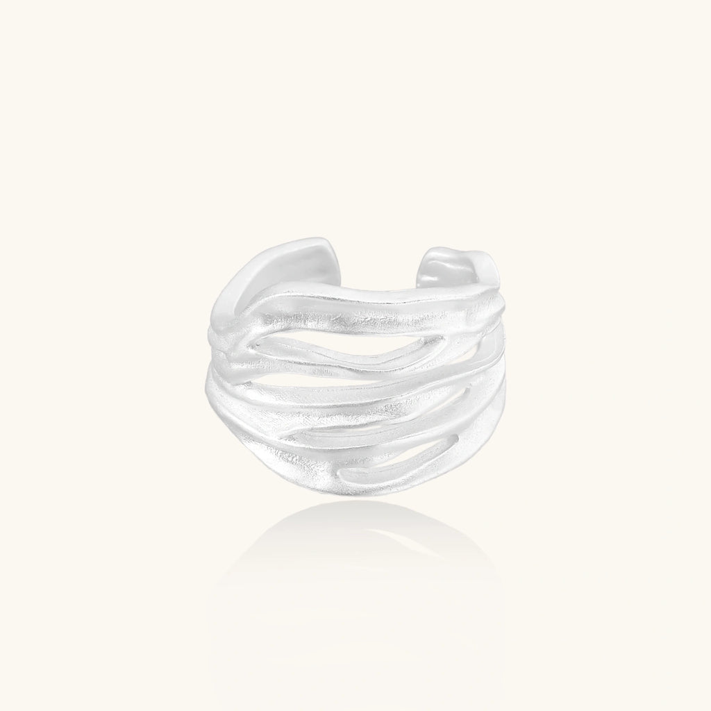 Wide sterling silver cuff ring with flowing wave patterns creating dimensional texture against cream background
