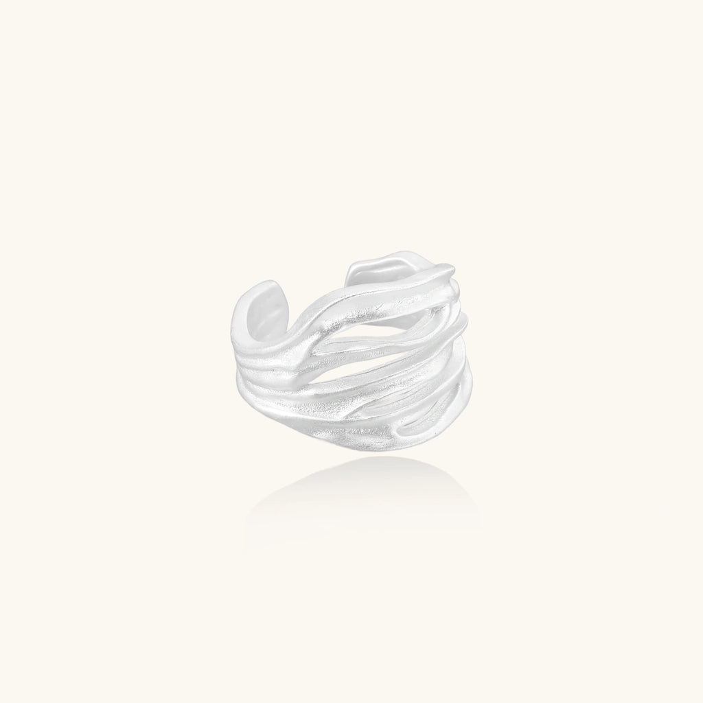 Wide sterling silver cuff ring with flowing wave patterns creating dimensional texture against cream background